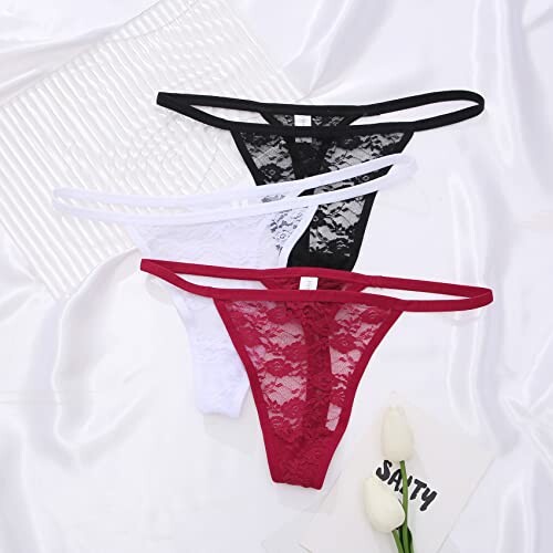 Conjunto de tangas de encaje en negro, blanco y rojo sobre tela blanca.